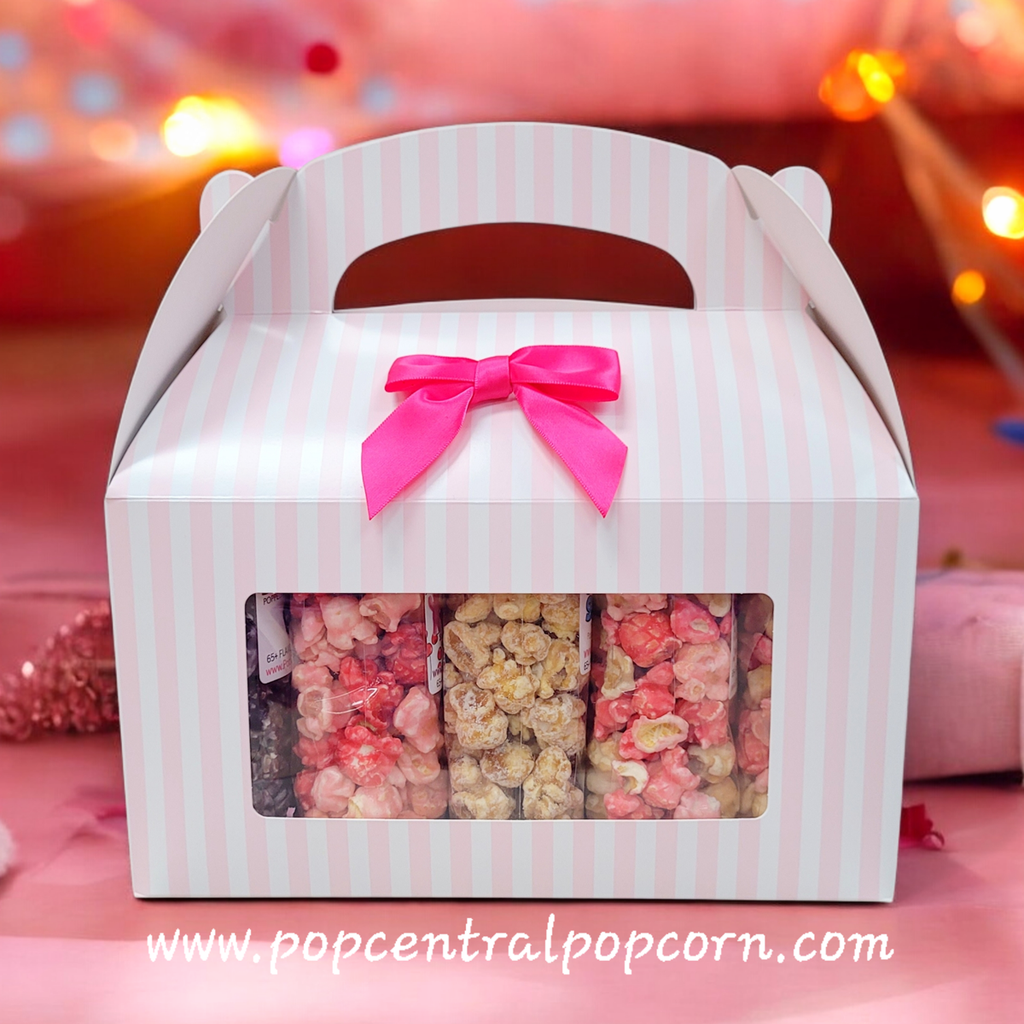 Striped popcorn box with pink bow and window displaying popcorn, on a blurred background.